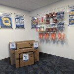A corner of the Defender Self Storage office that sells various moving supplies such as boxes sitting in a metal rack and things like locks and tape hanging up on metal retail shelving